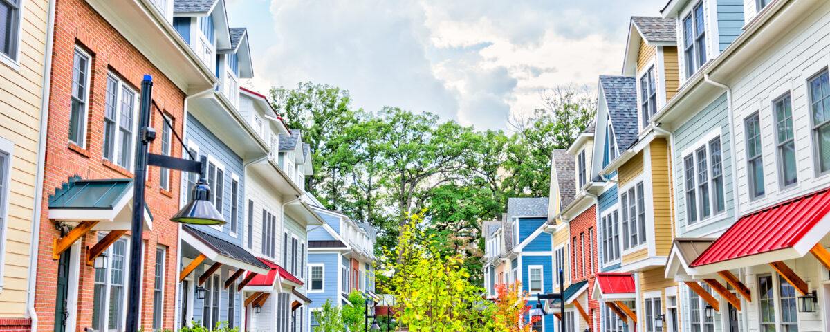 Row of colorful, red, yellow, blue, white, green painted residential townhouses, homes, houses with brick patio gardens in summer